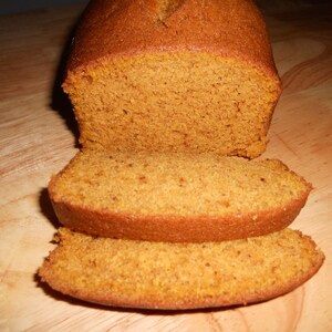 May include: A loaf of pumpkin bread sliced on a wooden chopping board. The bread is a light orange colour and has a soft, crumbly texture.