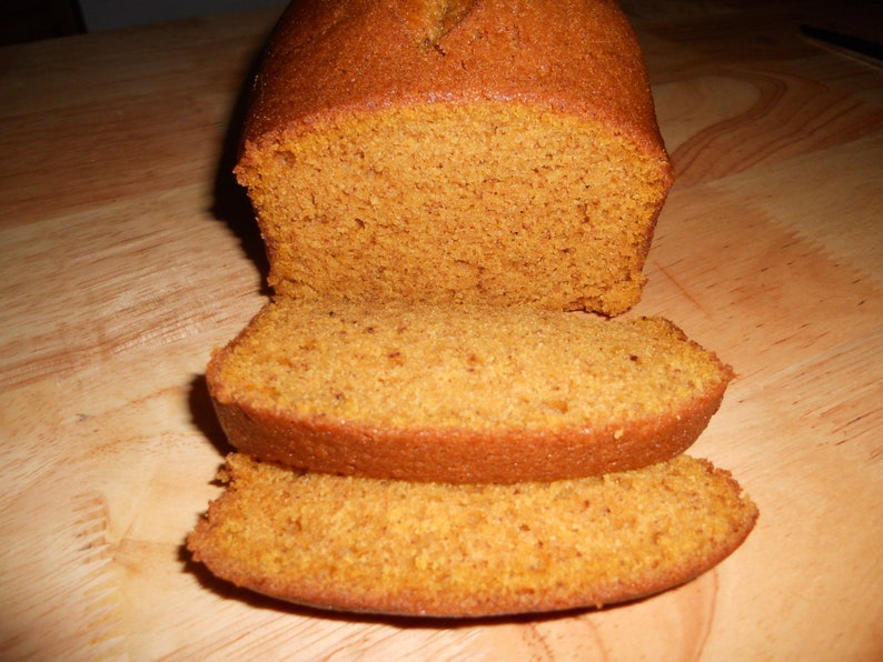 May include: A loaf of pumpkin bread sliced on a wooden chopping board. The bread is a light orange colour and has a soft, crumbly texture.