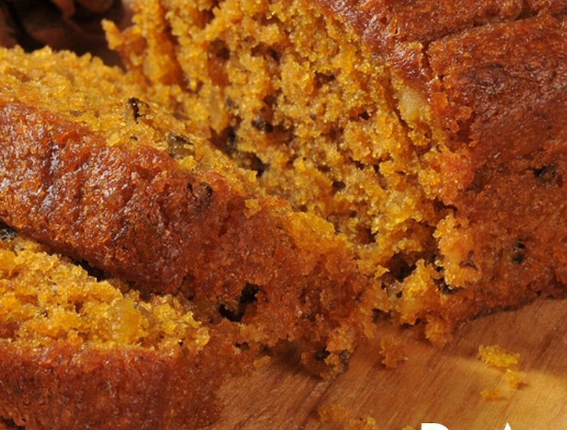 May include: A close-up of a loaf of pumpkin bread sliced into three pieces. The bread is a deep orange colour and has a crumbly texture. The bread is sitting on a wooden chopping board.