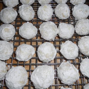 Puede incluir: Primer plano de una rejilla de alambre llena de bolas de nieve, un tipo de galleta, espolvoreada con az&uacute;car en polvo.