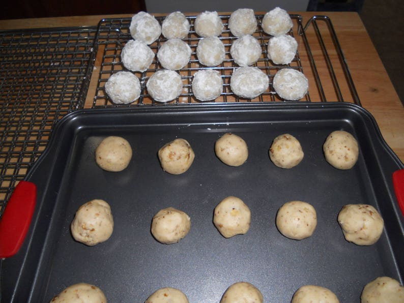 Puede incluir: Una bandeja para hornear con una superficie antiadherente negra contiene 12 bolas de masa sin hornear. Las bolas de masa est&aacute;n dispuestas en tres filas de cuatro. La bandeja para hornear est&aacute; sobre una superficie de madera.