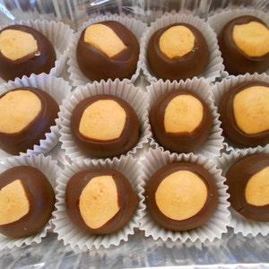 May include: A close-up of a dozen chocolate buckeyes, a popular Ohio candy, arranged in white paper cups. Each buckeye is a round ball of peanut butter covered in chocolate.