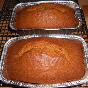 May include: Two loaves of freshly baked pumpkin bread in foil loaf tins on a wire rack.