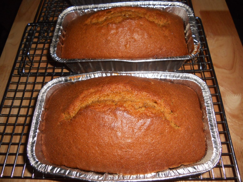 May include: Two loaves of freshly baked pumpkin bread in foil loaf tins on a wire rack.
