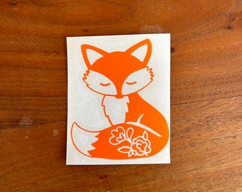 May include: Orange fox sticker with closed eyes and a floral design on its tail. The sticker is on a white background.