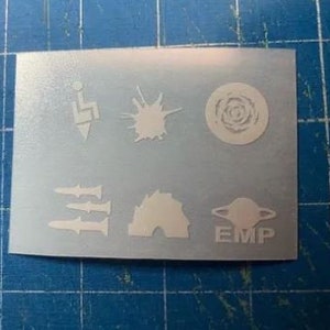 May include: A sheet of white vinyl stickers with various symbols, including a lightning bolt, a starburst, a circle with a swirl design, three missiles, a dome, and a planet with the word "EMP" underneath.