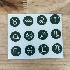 May include: A sheet of green and white stickers featuring the twelve zodiac signs. Each sign is depicted in a white outline on a dark green circle.