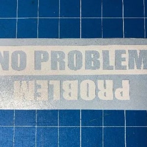 May include: A rectangular sticker with the words "NO PROBLEM" in large, block letters. Below, the same words are printed in reverse. The sticker is light gray with a white border, set against a blue grid background.