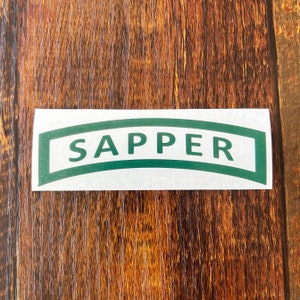 May include: A white sticker with a green arched border and the word "SAPPER" in green letters.