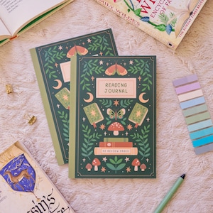 May include: Two green reading journals with a nature-themed design featuring butterflies, mushrooms, and the text "READING JOURNAL." The journals have a light green border and are surrounded by books, paper clips, and sticky notes.