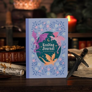 May include: A light blue reading journal with a dark teal oval centre featuring three dragons in purple, pink, and orange. The cover displays the text Reading Journal 50 Review Pages, surrounded by a decorative border of blue vines and small flowers.
