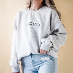 Pode incluir: Uma camisa de moletom cinza com o texto "From where you are planted" em letras pretas.
