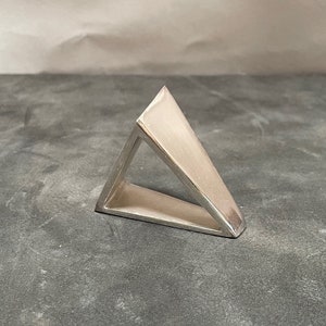May include: A silver triangle ring with a hollow center. The ring is made of a smooth, polished metal.