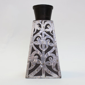 May include: A black and silver decorative vase with a geometric design. The vase has a wide base and a narrow neck.