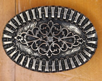 May include: A silver oval belt buckle with a black filigree design.