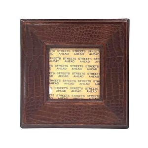 Könnte beinhalten: Ein brauner Lederbilderrahmen mit einer goldfarbenen Inschrift, die mehrmals "Streets Ahead" wiederholt. Der Rahmen hat ein Krokodilprägemuster.