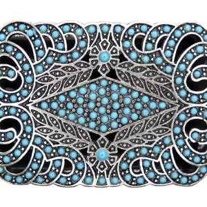 Puede incluir: Una hebilla de cinturón plateada con un diseño decorativo con piedras de color azul turquesa. La hebilla tiene un patrón floral detallado y una forma de diamante central.