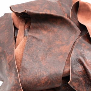 May include: A collection of dark brown leather scraps featuring a mottled, marbled texture with lighter reddish-brown highlights. The pieces show a smooth, finished grain on the top side and a soft, fibrous suede texture on the underside.