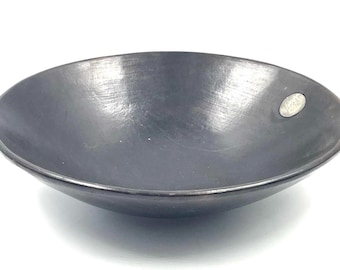 May include: A black ceramic bowl with a slightly rounded rim. The bowl has a smooth, glossy finish and a small, round sticker on the side.