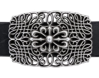 May include: A silver belt buckle with an intricate design featuring a cross-shaped motif in the center. The buckle is attached to a black leather belt.
