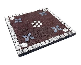 May include: A brown square coaster with a silver border and a repeating pattern of silver stars and seashells.