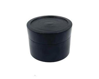May include: A black cylindrical container with a smooth, slightly textured lid. The container is made of wood and has a simple, elegant design.