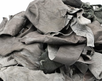 May include: A pile of irregular, soft grey leather scraps with visible natural grain and texture. The pieces vary in size and shape, displaying a matte finish with some edges showing a lighter, suede-like underside and others with a smooth surface.