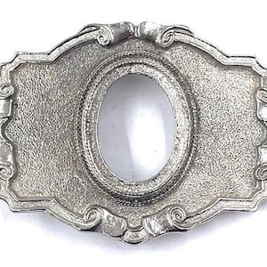 Puede incluir: Un marco de metal plateado con una abertura ovalada en el centro. El marco tiene un diseño decorativo con volutas y espirales alrededor de los bordes.