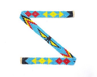 May include: A blue beaded strap with a geometric pattern in red, yellow, and black. The strap is shaped like the letter Z.