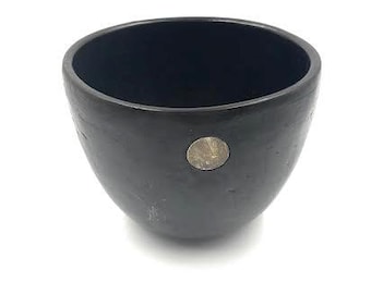 May include: A black ceramic planter with a round shape and a small gold sticker on the side.
