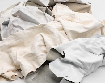 May include: A collection of assorted leather scraps in various shades of white, off-white, and cream. The pieces feature irregular shapes and textures, showcasing both the smooth finished grain side and the soft, fibrous suede underside of the material.