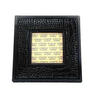 May include: A black picture frame with a crocodile-embossed design. The frame has a smaller inner frame with a yellow background and the text "Streets Ahead" repeated multiple times.