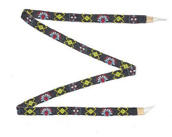 May include: A black beaded ribbon with a repeating geometric pattern in yellow, red, blue, and white. The ribbon is tied in a knot at the end.