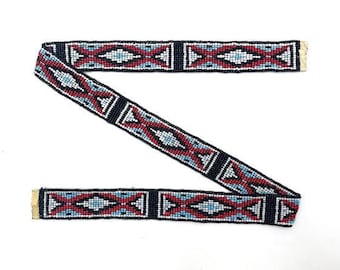 May include: A beaded trim with a geometric pattern in black, white, red, and blue. The trim is made of small beads sewn together in a repeating pattern.