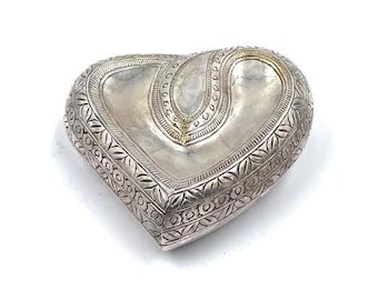 Puede incluir: Una caja de alhajas de plata en forma de corazón con intrincados diseños florales y geométricos. La caja tiene una sección central ligeramente elevada y un acabado liso y pulido.
