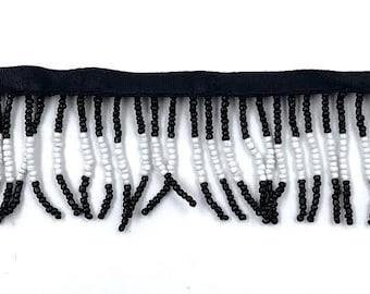 May include: Black and white beaded fringe trim. The fringe is made of small black and white beads that are strung together to create a tassel-like effect. The trim is approximately 1 inch wide.