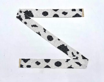 May include: A long, white beaded belt with a black and white cow print pattern.