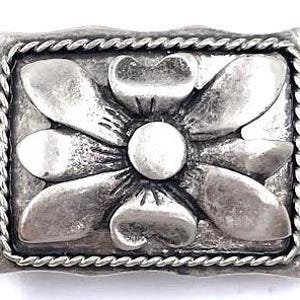 May include: Silver-toned metal belt buckle with a raised floral design. The buckle has a rope-like border.