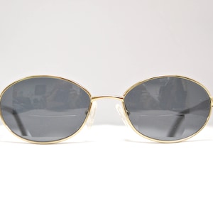 May include: Gold-rimmed oval sunglasses with dark gray lenses.