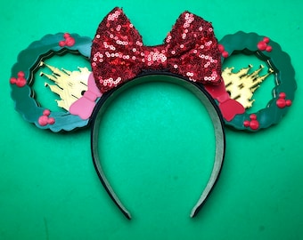 May include: Green and red Minnie Mouse ears with a red sequined bow and a gold castle silhouette inside a green wreath.