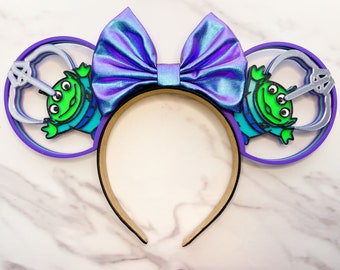 May include: Purple and blue iridescent bow headband with green alien character ears. The ears are layered with purple, silver, and white circles.