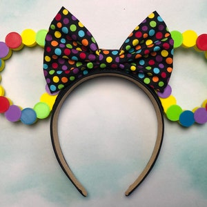 May include: A pair of black mouse ears with a colorful polka dot bow. The ears are made of foam circles in yellow, green, blue, purple, and red.