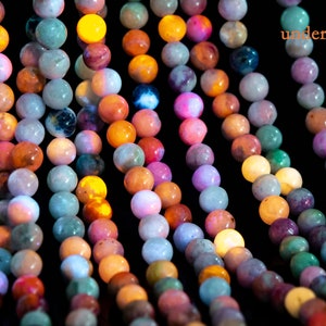 May include: A strand of colorful gemstone beads glowing under UV light. The beads are round and have a variety of colors, including green, blue, pink, and orange.