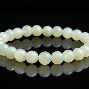 May include: A white beaded bracelet made of round, smooth stones. The bracelet is on a black background.