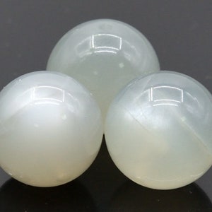 May include: Three white moonstone spheres, each with a smooth, polished surface and a subtle iridescent sheen.