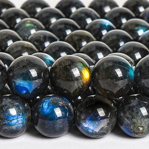 May include: A close-up of a strand of dark blue labradorite gemstone beads. The beads are round and have a smooth, polished finish. The labradorite has a beautiful iridescent sheen, with flashes of blue, green, and gold.