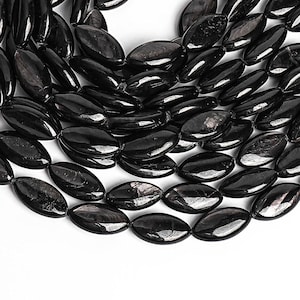 May include: A strand of black gemstone beads with a smooth, oval shape. The beads have a subtle shimmer and are strung together on a clear thread.