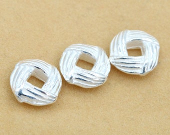 May include: Three silver-toned metal beads with a square-shaped hole in the centre. Each bead has a woven or braided design.