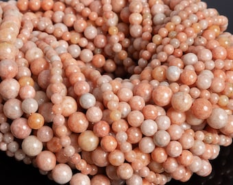 Könnte beinhalten: Nahaufnahme von Strängen aus pfirsichfarbenen Edelsteinperlen. Die Perlen variieren in der Größe und erzeugen ein strukturiertes Aussehen. Die Farbpalette umfasst Pfirsich-, Creme- und hellorangefarbene Töne. Diese Perlen eignen sich für die Schmuckherstellung.