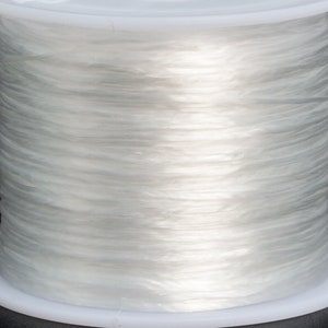 May include: A spool of clear elastic string wound around a white plastic bobbin. The string is translucent and appears to be very thin.